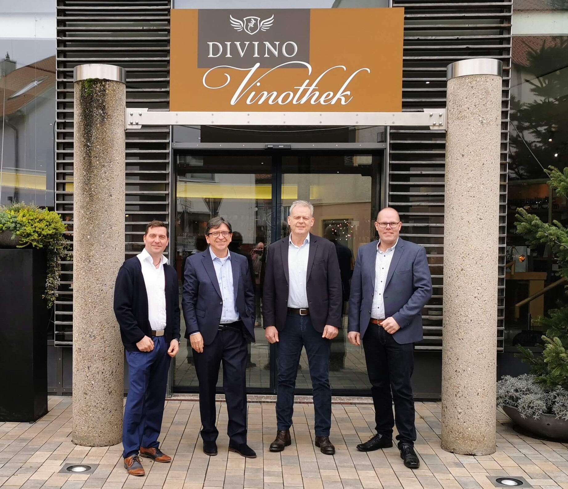 Pressefoto mit fünf Personen vor dem Eingang der Divino-Vinothek mit Logo-Schild.